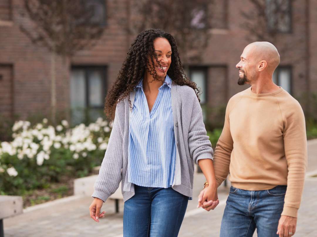 Young couple walking hand in hand smiling and laughing down a residential street at Brabazon. 