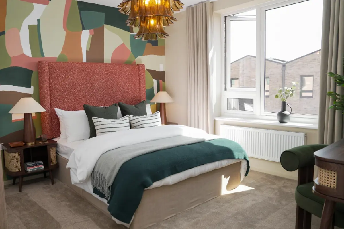 A stylish primary bedroom at Brabazon, featuring a textured orange headboard, colourful mural, cozy bedding, and a large window with natural light.