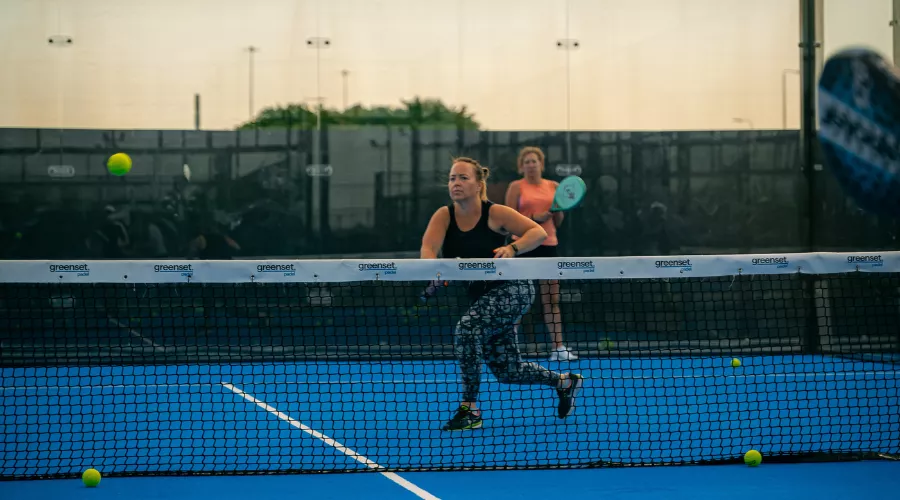 Woman running after a ball with her racket raised during a Padel game.