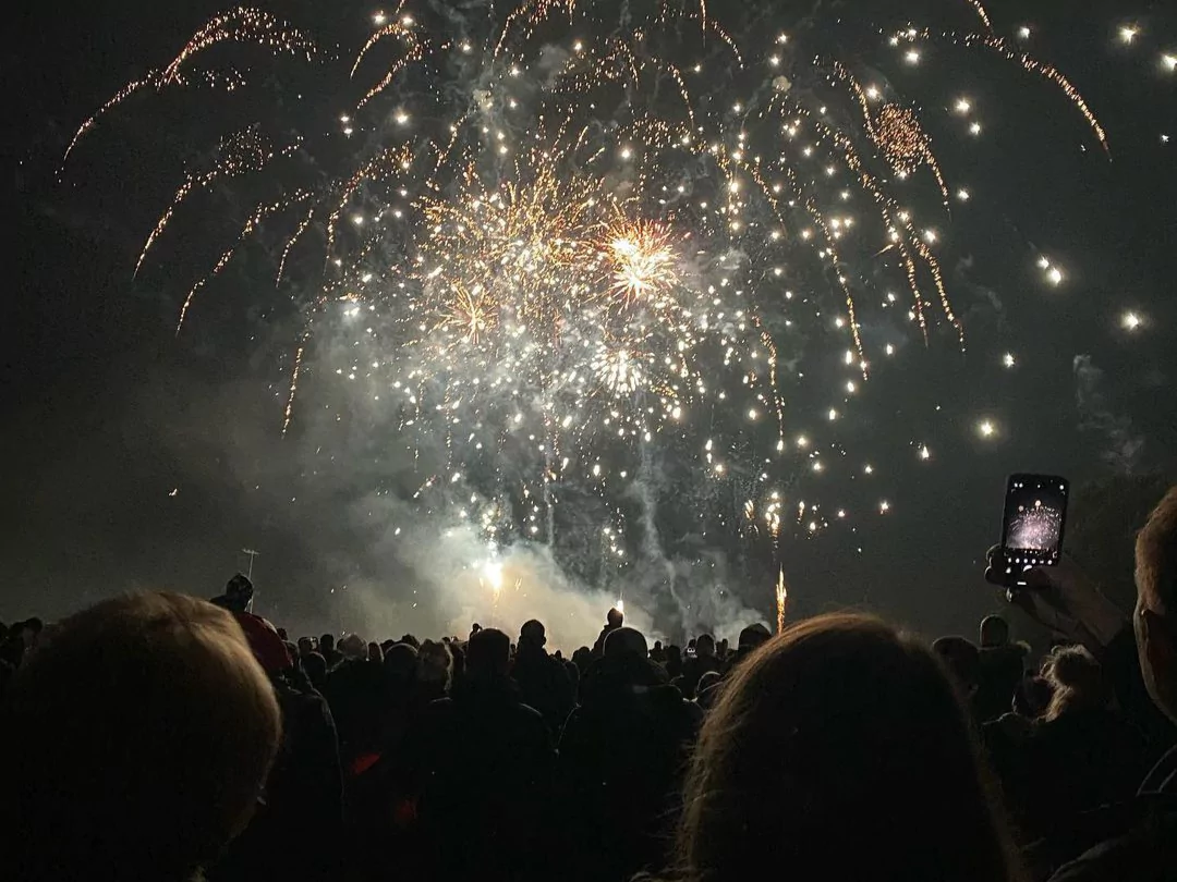 White and yellow fireworks exploding over the heads of a busy crowd.