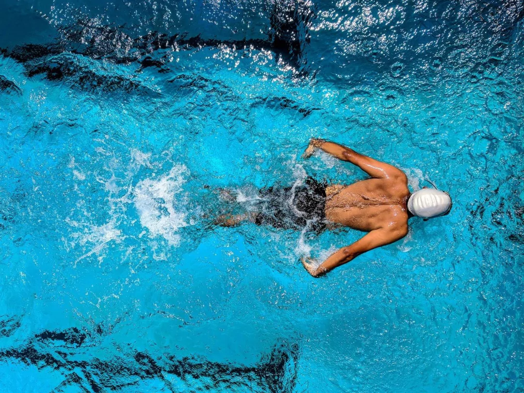 Muscular male swimmer in swimming hat doing butterfly stroke in a swimming pool.