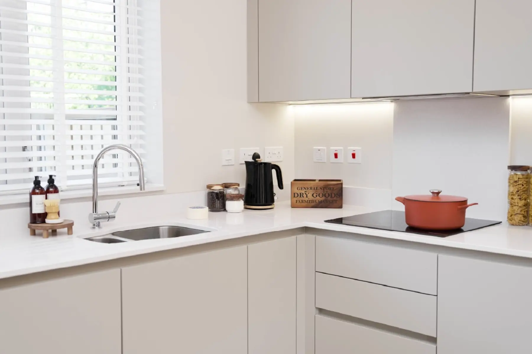 Modern kitchen at Brabazon with white cabinetry, a sink, kettle, and a red pot on the stovetop, featuring natural light and organized shelves.