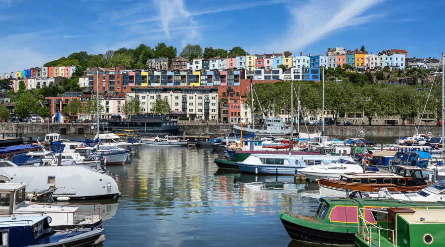 Bristol Harbourside, with colourful house boats lined up at a jetty, and colourful houses on the hill.