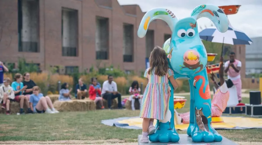 Young girl hugs large blue Gromit Sculpture while watching performance at Brabazon.
