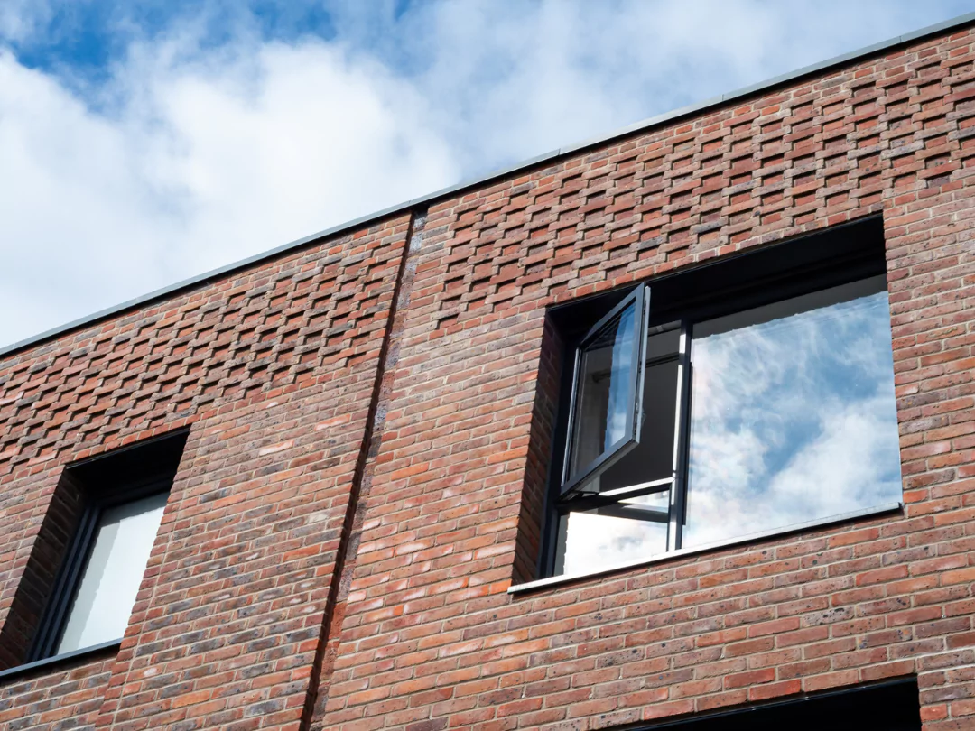 Close up of large picture window of a modern brick terrace house, with a partly cloudy sky in the window's reflection. 